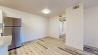This single-floor unit offers a clean, modern aesthetic defined by light wood-style flooring that extends seamlessly throughout every room, creating a cohesive and airy feel. The open kitchen is well-appointed with crisp white cabinetry, stone-look countertops, a stainless steel refrigerator, dishwasher, and range, along with a double-basin sink positioned beneath a window with vertical blinds that allow in natural light. A peninsula counter provides additional workspace and enhances the open flow between the kitchen and living areas. The living space features a ceiling fan and sliding glass doors that open to an outdoor area, filling the room with abundant natural light and views of the surroundings. Multiple generously sized rooms offer flexibility, each featuring the same durable light wood-style flooring and bright white walls that lend a fresh, neutral palette. The bathroom is finished with a single-sink vanity topped with a speckled countertop and a large mirror, complemented by matching light flooring. A dedicated laundry closet houses a top-loading washer and overhead shelving, adding practical convenience. Throughout the unit, ceiling-mounted light fixtures, HVAC vents, and clean wall finishes underscore the move-in-ready condition of this well-designed space.