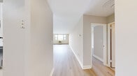 This 2-bedroom, 1-bathroom residence is thoughtfully laid out across a single floor, offering a clean, modern aesthetic throughout. Light wood laminate flooring runs continuously through the living areas, bedrooms, and hallway, creating a cohesive and airy feel. Neutral warm-toned walls complement the bright, open atmosphere.

The combined kitchen and living area provides a practical, open-concept arrangement. The galley-style kitchen is equipped with white cabinetry, dark countertops, a gas range, and a dishwasher, with tile flooring underfoot. A pass-through window connects the kitchen to the living room, enhancing the sense of openness.

The spacious living room receives generous natural light and offers a clean, versatile space. The primary bedroom is a well-proportioned room featuring a wide window with scenic views of greenery and water, a wall-unit air conditioner, and a mirrored sliding closet. The second bedroom similarly benefits from window views and light wood flooring.

The bathroom is finished with neutral tile surrounding the shower-tub combination, a white vanity with under-cabinet storage, and a wall mirror. A central hallway connects all rooms efficiently. Throughout the residence, white trim and baseboards provide a crisp, polished finish.