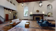 Located at 6500 Yucca St in the heart of Hollywood, this single-floor space showcases a striking Spanish Colonial Revival aesthetic that commands attention from the moment you enter. The centerpiece is a dramatic great hall with soaring cathedral-height ceilings adorned with richly stained wood coffered panels and ornate wrought-iron chandelier fixtures that cast warm, ambient light throughout. Expansive terracotta tile floors in a classic diamond-set pattern extend across all areas, lending a cohesive and timeless character to the interior.

A grand fireplace with decorative Talavera-style tilework serves as a focal point in the main hall, framed by a dark wood mantel and accented by a sunburst mirror above. Tall arched windows allow natural light to filter in, illuminating the crisp white walls and highlighting the architectural depth of the space. Graceful white archways supported by sturdy columns define the circulation corridors, creating a rhythm of open, interconnected areas.

Additional rooms branch off from the main hall, each maintaining the same terracotta flooring and arched detailing. A dark wood-paneled anteroom with a coffered ceiling offers a more intimate atmosphere. Throughout, built-in niches, red-painted doors, and carefully placed wall sconces contribute to the space's rich historical character and refined ambiance.