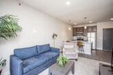This well-appointed single-floor unit offers a thoughtfully designed open-concept layout that seamlessly connects the living area to the kitchen. The living room features plush carpeting, generous natural light, and sliding glass doors that open onto a private balcony, providing pleasant outdoor views. The kitchen is a standout space, equipped with stainless steel appliances including a refrigerator, range, and microwave, complemented by rich dark wood cabinetry and a granite-topped peninsula with bar seating and pendant lighting overhead. Wood-look flooring runs throughout the kitchen and entry areas, adding warmth and continuity. The primary bedroom is bright and comfortable, featuring a ceiling fan, carpeted floors, and windows with views, as well as direct access to the balcony. A second bedroom offers a cozy and quiet retreat with soft carpet and neutral tones. The full bathroom is finished with granite countertops, dark wood cabinetry, a combined tub and shower, and wood-look flooring. Throughout the unit, neutral wall tones, recessed lighting, and clean architectural lines create a cohesive, modern aesthetic that is both functional and inviting.