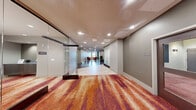 Located at 272 E Main St in downtown Rochester, NY, this impressive single-floor amenity space offers a thoughtfully designed environment spanning a generously sized footprint. The layout is anchored by a sophisticated living room featuring coffered ceilings, a striking globe chandelier, and large windows that flood the area with natural light while framing views of the city skyline. Rich hardwood flooring and a vibrant, multicolored area rug in warm orange and violet tones lend a contemporary flair, complemented by plush leather seating, a glass coffee table, and a dining area with modern chairs.

Floor-to-ceiling glass partitions divide the space elegantly, creating distinct zones while preserving an open, connected atmosphere. A library nook and additional lounge seating areas provide quiet retreats, while wide corridors with polished floors connect each section seamlessly. A dedicated screening room outfitted with reclining leather theater seats and cinema-themed décor offers an intimate entertainment experience.

The fitness center is well-appointed with cardio machines—including treadmills, ellipticals, and a stair climber—alongside free weights and a weight bench. Mirrored walls, wood-paneled accents, and windows overlooking the street enhance the workout environment. Together, these amenities create a dynamic, upscale communal space designed for both relaxation and an active lifestyle.
