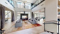 Located at 120 Commerce Way in Woburn, Massachusetts, this expansive amenity floor offers a thoughtfully designed collection of communal spaces that blend modern aesthetics with functional comfort. The grand lobby anchors the space with soaring double-height ceilings, a dramatic open staircase with wood treads and glass railings, and polished concrete flooring that transitions seamlessly into herringbone-patterned hardwood throughout the interior. Floor-to-ceiling windows flood the space with natural light and provide views of the surrounding exterior courtyard and parking areas. A spacious lounge area features a striking floor-to-ceiling marble fireplace, plush sectional seating, and bold accent rugs, creating a welcoming social atmosphere. Adjacent to the lounge, a dedicated game room is equipped with a billiards table, shuffleboard, and high-top seating beneath an elegant coffered ceiling. The bar and dining area showcases dark subway tile, a granite-topped bar with modern stools, globe pendant lighting, and an intimate curved banquette with rich green velvet upholstery. A co-working area provides functional workstations and conference-style seating alongside a mail center. Built-in shelving, decorative wall art, and carefully curated furnishings throughout contribute to the space's polished, contemporary character.