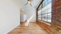 Located at 1514 E Cleveland Ave in East Point, Georgia, this three-bedroom, one-bathroom unit blends industrial character with modern finishes across a single floor. Warm-toned hardwood-style flooring runs throughout, complementing the neutral wall palette and creating a cohesive, inviting atmosphere. Soaring ceilings amplify the sense of space in each room, while large, multi-pane windows framed by exposed red brick accent walls flood the bedrooms with abundant natural light and views of the surrounding neighborhood. The primary bedroom offers a generous footprint and includes a dedicated closet with built-in shelving, accessed through classic double doors. The additional bedrooms share the same elevated ceiling height and bright, airy feel. The kitchen is well-appointed with granite-style countertops, a peninsula breakfast bar, warm taupe cabinetry, stainless steel appliances including a gas range, microwave, dishwasher, and refrigerator, and a double-basin sink. The full bathroom features a tub-shower combo and clean, white finishes with modern grab bar hardware. A dedicated laundry room with washer and dryer hookups adds everyday convenience, rounding out this thoughtfully designed urban residence.