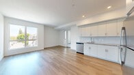 Located on the fourth floor at 18900 Parthenia St in the Northridge neighborhood of Los Angeles, this thoughtfully designed 2-bedroom, 1-bathroom unit offers a clean, contemporary aesthetic throughout. Warm wood-style flooring flows consistently across the living areas, kitchen, bedrooms, and hallway, creating a cohesive and inviting atmosphere.

The open kitchen and living area form the heart of the unit. The kitchen is well-appointed with white shaker-style cabinetry, granite-look countertops, a subway tile backsplash, and a full suite of stainless steel appliances including a refrigerator, range, over-the-range microwave, and dishwasher.

Both bedrooms are bright and airy, each featuring large windows that invite natural light and offer views of the surrounding neighborhood. The primary bedroom is a comfortable size with ample space for furnishings. A dedicated walk-in closet provides generous storage with built-in shelving and hanging rods.

The bathroom is finished with large-format tile flooring, a granite-topped vanity with modern cabinetry, a lighted mirror, and a full soaking tub with tiled surround. A clean hallway connects the private and shared spaces efficiently. The unit's white walls, recessed lighting, and modern finishes throughout contribute to a bright, move-in-ready living environment.