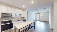 This single-floor residence presents a clean, contemporary design throughout. The kitchen serves as a central highlight, outfitted with white shaker-style cabinetry extending to the ceiling, granite countertops, a subway tile backsplash, and a full suite of stainless steel appliances including a refrigerator, range, microwave, and dishwasher. A freestanding kitchen island provides additional prep and dining space, while wood-look flooring ties the kitchen seamlessly into the open living area. The living space benefits from natural light through large windows and a glass door that opens to the outdoors, complemented by a ceiling fan overhead.

The unit includes two bathrooms: one featuring a glass-enclosed walk-in shower with vertical tile detailing, and a second with a tiled shower-tub combination and a granite-topped vanity. Both bathrooms feature wood-look flooring and clean white finishes. Bedrooms are carpeted and include generous closets with wire shelving systems and natural light from windows. A dedicated laundry area houses a full-size side-by-side washer and dryer with overhead storage shelving, adding everyday convenience to this well-appointed home.