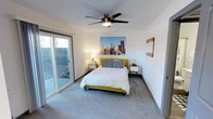 This single-floor space offers a clean, modern aesthetic with a comfortable and functional layout. The bedroom is a standout feature, showcasing crisp white walls that create a bright and airy atmosphere. Soft, wall-to-wall carpeting underfoot adds warmth and comfort to the room. A ceiling fan with a sleek, low-profile design is centrally mounted, providing both air circulation and a subtle contemporary accent overhead. Large sliding glass doors along one wall flood the room with natural light and provide direct access to an outdoor area, where lush greenery is visible — creating a seamless connection between interior and exterior living spaces. The room also features a dedicated wall-mounted accent piece, adding a touch of rustic charm against the otherwise minimalist backdrop. The overall ambiance of the space is calm, uncluttered, and inviting, with a mid-century modern sensibility reflected in its clean lines and understated design choices. The single-floor layout ensures ease of movement throughout, making the space practical as well as aesthetically pleasing. Natural light, outdoor views, and thoughtful design details come together to create a welcoming and well-balanced living environment.