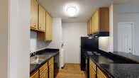 This single-floor, two-bedroom, one-bathroom residence in Little Rock, Arkansas offers a practical and well-organized layout. The galley-style kitchen is efficiently designed with warm oak cabinetry lining both walls, dark granite-look countertops, black appliances including a range and refrigerator, a stainless steel sink, and wood-look flooring. A stacked washer and dryer unit is conveniently housed within the kitchen area. The open living area features neutral-toned carpet, a ceiling fan with light fixture, and direct sightlines to the kitchen, creating a cohesive and connected common space. A sliding glass door in one area of the unit allows natural light to filter in and provides outdoor access. Both bedrooms are carpeted and finished with neutral walls and textured ceilings. Each room benefits from windows with blinds that bring in natural light, and at least one bedroom includes a walk-in closet for added storage. The bathroom is clean and straightforward, featuring a full tub-shower combination, toilet, and dark countertop vanity with wood-look flooring that ties back to the kitchen aesthetic. Overall, the residence offers a comfortable and functional living environment suitable for everyday living.