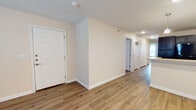This single-floor residence presents a well-designed layout with a clean, contemporary aesthetic throughout. Warm wood-look luxury vinyl plank flooring flows consistently across all main living areas, complemented by neutral-toned walls and crisp white trim and doors that create a bright, cohesive interior.

The entry opens into a spacious hallway corridor, providing access to the various rooms of the home. The open living area is generously sized, featuring recessed lighting, a ceiling fan with light fixture, and ample room for flexible furniture arrangements.

The kitchen is a standout feature, outfitted with dark espresso cabinetry, black appliances including a refrigerator, range, and microwave, and light-toned countertops. A peninsula with pendant lighting above offers additional prep space and a casual dining option, while a tall pantry cabinet provides substantial storage.

The bedrooms are well-proportioned with neutral walls and large windows fitted with blinds that allow natural light to filter in. Two full bathrooms serve the home: one includes a tub-shower combination with full white tile surround and a dark vanity with a light countertop, while the other features a glass-enclosed walk-in shower with white tile walls and beige tile flooring throughout both bathrooms.