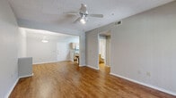 This single-floor, one-bedroom, one-bathroom unit offers a functional and well-organized layout. The combined living and dining area serves as the central gathering space, featuring warm hardwood-style flooring, neutral gray walls, a textured ceiling, and a ceiling fan with integrated lighting. A sliding glass door leads to a private balcony, allowing natural light to fill the space and providing outdoor views. An adjacent dining area includes a pendant light fixture overhead.

The galley-style kitchen runs parallel along one side of the unit, equipped with light wood cabinetry, granite-style countertops, white appliances including a range and refrigerator, and a double-basin sink. A dedicated laundry area is accessible directly from the kitchen. A separate dining nook with hardwood-style flooring and a flush-mount ceiling light connects the kitchen to the main living space.

The bedroom is carpeted and comfortably sized, featuring a ceiling fan, a window with blinds that brings in natural light, and access to a dedicated closet. The full bathroom includes a tub/shower combination with tile surround, a vanity with granite-style countertops, light wood cabinetry, and hardwood-style flooring throughout.