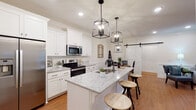 Located on Ray Williams Drive in Spring Hill, Tennessee, this single-story home showcases a cohesive modern farmhouse aesthetic carried throughout every room. The open-concept kitchen is a standout feature, outfitted with crisp white shaker cabinets, light granite countertops, stainless steel appliances, and a central island with a built-in sink illuminated by a trio of striking black geometric pendant lights. Warm hardwood flooring flows seamlessly into the adjacent dining area, where wainscoting, crown molding, and a classic black chandelier add refined character. A sliding white barn door connects the kitchen and dining space, reinforcing the home's farmhouse charm. The living room is bright and welcoming, with natural light pouring in through large windows and a glass door, complemented by crown molding and a ceiling fan. The bedroom offers a tranquil retreat with crown molding, recessed lighting, and a ceiling fan, while a second flexible room functions well as a guest space or home office. The bathroom features white cabinetry with granite countertops, a large vanity mirror, and warm hardwood floors. A dedicated laundry room with full-size washer and dryer adds everyday convenience to this well-appointed Spring Hill home.