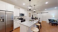 Located on Ray Williams Drive in Spring Hill, Tennessee, this single-story home showcases a cohesive modern farmhouse aesthetic carried throughout every room. The open-concept kitchen is a standout feature, outfitted with crisp white shaker cabinets, light granite countertops, stainless steel appliances, and a central island with a built-in sink illuminated by a trio of striking black geometric pendant lights. Warm hardwood flooring flows seamlessly into the adjacent dining area, where wainscoting, crown molding, and a classic black chandelier add refined character. A sliding white barn door connects the kitchen and dining space, reinforcing the home's farmhouse charm. The living room is bright and welcoming, with natural light pouring in through large windows and a glass door, complemented by crown molding and a ceiling fan. The bedroom offers a tranquil retreat with crown molding, recessed lighting, and a ceiling fan, while a second flexible room functions well as a guest space or home office. The bathroom features white cabinetry with granite countertops, a large vanity mirror, and warm hardwood floors. A dedicated laundry room with full-size washer and dryer adds everyday convenience to this well-appointed Spring Hill home.