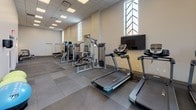 Located at 538-546 Broad Street in Newark, NJ, this fitness and yoga center offers a thoughtfully designed, single-floor facility built to support a comprehensive workout experience. The gym floor is finished with durable large-format tile and rubber flooring, providing a clean and functional foundation throughout the space.

The cardio area is outfitted with treadmills, stationary bikes, and elliptical machines, all arranged to allow ample room for comfortable use. Strength training is well supported with a multi-station cable machine, adjustable benches, and a full rack of dumbbells spanning a range of weights. Wall-mounted flat-screen TVs are positioned throughout the space to keep members engaged during workouts.

The facility is illuminated by a combination of recessed ceiling panels and natural light streaming through tall, decorative arched windows, lending the space an open and airy feel. The neutral color palette of warm whites and grays contributes to a clean, modern aesthetic.

A dedicated hydration alcove is built into the wall, housing a dual-level water fountain and bottle-filling station, conveniently located near the free weight area. The layout is spacious and well-organized, accommodating a variety of fitness activities with clear circulation paths between equipment zones. This center provides a complete and accessible environment for both cardio and strength-focused training.