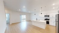 Located at 402 Fast Ln in Hudson, Iowa, this modern 2-bedroom, 3-bathroom multi-floor home is thoughtfully designed across three levels. The ground floor entry features a clean, light-filled foyer with light wood flooring and dark-carpeted stairs with a sleek metal handrail leading to the main living level.

The main floor is anchored by a bright, open-concept kitchen and living room. The kitchen is outfitted with crisp white shaker cabinetry, a large center island with an integrated sink and black fixtures, stainless steel appliances, and stylish pendant lighting. Light wood flooring flows seamlessly into the spacious living area, which opens to a private balcony through sliding glass doors, allowing abundant natural light and neighborhood views.

The upper floor houses both bedrooms and the remaining bathrooms. The generously sized primary bedroom offers a comfortable retreat, while the second bedroom features a large window with natural light and neighborhood views. Closet space is provided in the bedrooms for practical storage. The three bathrooms are finished in a clean, neutral palette with light wood-look flooring, including a walk-in shower unit and a separate bathroom with a soaking tub and natural light from a window. Throughout the home, white walls, recessed lighting, and consistent flooring create a cohesive, modern aesthetic.