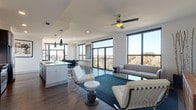 This stylish 2-bedroom, 2.5-bathroom residence offers a thoughtfully designed open-concept layout with contemporary finishes throughout. The expansive living area is anchored by large floor-to-ceiling windows framed in sleek black, flooding the space with natural light and offering sweeping outdoor views. A ceiling fan overhead and rich hardwood-style flooring add warmth and comfort to the living room, which flows seamlessly onto a private balcony.

The kitchen is a standout feature, showcasing grey cabinetry, a white quartz waterfall island with seating for three, stainless steel appliances, and elegant pendant lighting. A tasteful tile backsplash and ample storage complete this well-appointed space.

Both bedrooms are generously sized, each with direct balcony access through black-framed glass doors, offering bright views of the surrounding landscape and cityscape. The primary bathroom features marble-look tile flooring, a dark-cabinetry vanity with a white countertop, and a walk-in closet. The second full bathroom mirrors this refined aesthetic with clean white surfaces and a tiled shower surround. A convenient half bath rounds out the layout. Throughout, the design maintains a cohesive modern palette of whites, greys, and natural wood tones.