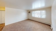 This single-floor unit offers a straightforward and functional layout designed for comfortable everyday living. The living area is generously sized, finished with neutral wall-to-wall carpeting and clean white walls that create a bright, open atmosphere. A large window allows natural light to fill the room, complemented by a baseboard heating system and a wall-mounted air conditioning unit for year-round climate control. Adjacent to the living area, the kitchen features rich dark wood cabinetry, laminate countertops, a double-basin sink, and a ceiling fan with light fixture overhead. The hardwood-style flooring in the kitchen adds warmth and is easy to maintain. The bedroom is a comfortable, carpet-floored space with its own window offering outdoor views and a baseboard heater for added comfort. The full bathroom is cleanly designed with white tile walls, a vanity with under-sink cabinet storage, a mirrored medicine cabinet, and a combined tub and shower. The overall layout, as seen in the floor plan view, is compact yet efficiently organized, making excellent use of the available space. The unit's clean, neutral palette provides a versatile backdrop ready for personalization.