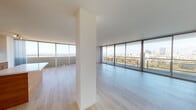 Located along the Lake Merritt Path in Oakland, CA, this single-floor residence is situated at an elevated position within its building, offering sweeping panoramic views of the Oakland skyline, Lake Merritt, and the surrounding Bay Area landscape. The open-concept living and dining areas are defined by expansive floor-to-ceiling sliding glass doors and windows that wrap around multiple sides of the space, flooding the interiors with abundant natural light and providing direct access to a generous balcony. Light-toned hardwood flooring runs throughout the main living areas, complementing the clean, contemporary aesthetic.

The kitchen is well-appointed with warm wood-grain cabinetry extending to the ceiling, white quartz countertops, a glossy white subway tile backsplash, stainless steel appliances including a french-door refrigerator and dishwasher, and a large single-basin sink. A peninsula with additional storage connects the kitchen to the open living space.

The bathrooms echo the modern design language, featuring wood-grain vanity cabinetry with open shelving, white quartz countertops, undermount sinks, large frameless mirrors, and clean white walls. The overall ambiance of the space is bright, minimalist, and urban, with the ever-present backdrop of Oakland's dynamic cityscape enhancing every room.