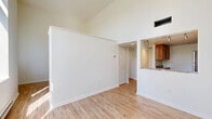 Located at 500 Tripoli Street in Pittsburgh's North Side, this one-bedroom, one-bathroom unit offers a thoughtfully designed layout across a single floor. The living room immediately impresses with its soaring vaulted ceilings that amplify the sense of space, complemented by large windows that frame lush outdoor greenery and flood the room with natural light. Light wood laminate flooring runs throughout, adding warmth to the bright, white interior. Decorative built-in wall niches provide a subtle architectural accent in the living area. The kitchen features warm wood cabinetry, a stone-style countertop, and an open pass-through bar connecting it to the living space, enhancing the open feel of the home. Track lighting illuminates the kitchen efficiently. A hallway with recessed lighting connects the main living areas to the private bedroom, which offers generous proportions, vaulted ceilings, and a large sliding double-door closet alongside a built-in dresser unit. Three closets total provide ample storage throughout. The bathroom is clean and functional, featuring a full-size soaking tub with an integrated shower surround and chrome fixtures. The overall ambiance is clean, airy, and modern, making efficient and stylish use of every square foot.