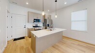 Located at 401 W Center St in Hyde Park, Utah, this two-story home offers a well-planned layout spread across two floors. The main level provides an open, light-filled living area anchored by a sleek, modern kitchen. The kitchen features taupe flat-front cabinetry, a large central island with a white quartz countertop, an undermount sink, stainless steel appliances including a gas range, refrigerator, and dishwasher, and pendant lighting overhead. Light hardwood flooring runs throughout the main level, complementing the bright white walls and creating a clean, contemporary aesthetic. A half bathroom on this floor features warm wood-toned cabinetry with black hardware and matching hardwood flooring. The upper level hosts both bedrooms, two full bathrooms, a hallway, and a dedicated laundry room. The generously sized primary bedroom includes its own walk-in closet with built-in shelving, hanging rods, and a natural light window. The second bedroom also features access to a closet with built-in shelving. The carpeted upper-level bedrooms provide a comfortable contrast to the hardwood below. The laundry room is equipped with a full-size washer and dryer, overhead cabinetry, and additional countertop space. Throughout the home, black hardware accents, recessed lighting, and a neutral palette contribute to a cohesive modern design.