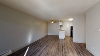This single-floor unit offers a well-organized layout designed for comfortable everyday living. The open-concept living area is finished with rich, dark hardwood-style flooring and features a ceiling fan overhead, creating a practical and inviting space. Neutral-toned walls and a textured ceiling carry throughout, lending a consistent and clean aesthetic across the unit.

The kitchen flows seamlessly from the living area and is equipped with white cabinetry, a peninsula with counter seating, a range with overhead ventilation, a black refrigerator, and a sink with ample counter space — providing everything needed for home cooking and casual dining.

The bedrooms are carpeted for added comfort and receive generous natural light through large windows that offer views of the surrounding neighborhood. Each bedroom includes closet storage, and one features dual doors providing access to both a closet and the hallway.

The bathroom is neatly appointed with wood-style flooring, a white vanity, a full-size soaking tub with a shower surround, and chrome fixtures, keeping the space bright and functional.

An additional room with light hardwood-style flooring, a wall-mounted HVAC unit, and a window provides flexible space suitable for use as a home office, den, or dining area. Baseboard heating is also present in select rooms, ensuring year-round comfort.