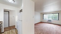 Located at 2105 Barton Avenue in West Bend, Wisconsin, this one-bedroom, one-bathroom unit offers a functional and well-organized single-floor layout. The galley-style kitchen is equipped with dark espresso cabinetry, granite-style countertops, a gas range, refrigerator, and double-basin sink, all set over light wood-look flooring. A chandelier overhead adds a touch of elegance to the combined kitchen and dining area, which transitions seamlessly into the main living spaces. The carpeted living room is bright and open, featuring a large window with vertical blinds, a baseboard heating system, and a wall-mounted air conditioning unit for year-round comfort. The generously sized primary bedroom also features plush carpeting, a wide window that invites natural light, baseboard heat, and a full-width closet with bi-fold doors — providing ample storage. Three closets total are distributed throughout the unit. The bathroom is finished with full-height stone-look ceramic tile surrounding the soaking tub and shower, complemented by wood-tone cabinetry and a granite-style vanity top. A connecting hallway ties all rooms together efficiently, completing this thoughtfully arranged living space.