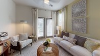 This single-floor residence presents a thoughtfully designed open-concept layout that seamlessly connects the main living areas. The living room is a welcoming space featuring large windows dressed with layered blinds and sheer curtains, allowing abundant natural light to fill the room. A ceiling fan overhead and decorative wall art add character, while light-toned walls contribute to an airy, relaxed atmosphere.

The kitchen is a functional and stylish centerpiece, featuring gray shaker-style cabinetry, granite countertops, and a full suite of stainless steel appliances, including a range, over-the-range microwave, and refrigerator. A peninsula with bar seating bridges the kitchen and living area, complemented by pendant lighting that enhances the open feel. Light wood-style flooring flows throughout the main living spaces.

The bedroom is comfortably sized with carpeted flooring, a ceiling fan, and a window that brings in natural light. Soft, neutral tones create a calm retreat. The bathroom includes a granite-topped vanity with gray cabinetry, a combination tub and shower, and wood-style flooring, maintaining the cohesive design aesthetic found throughout the residence.