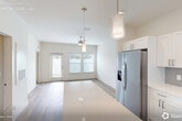 Located at 9000 Little Palm Way in Venice, FL, this thoughtfully designed single-story home offers a bright, modern interior with a clean, neutral palette throughout. The open-concept living and dining area is filled with natural light from multiple windows fitted with sleek blinds, and is complemented by light wood-look flooring and a ceiling fan. The well-appointed kitchen is a standout feature, showcasing white shaker cabinetry, quartz countertops, a gray subway tile backsplash, a stainless steel undermount sink, and a full suite of stainless steel appliances including a refrigerator with ice maker, electric range, built-in microwave, and dishwasher. A large island provides additional prep and dining space. The spacious bedroom benefits from abundant natural light through large windows, warm wood-look flooring, a ceiling fan, and access to a dedicated walk-in closet. The full bathroom features a white vanity with quartz countertop, a large mirror, and a glass-enclosed tiled shower. A separate laundry room houses a full-size washer and dryer. Outside, the property includes a generously sized, fully fenced backyard with vibrant artificial turf, offering a private and low-maintenance outdoor retreat.