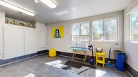 Located at 8885 W Thunderbird Rd in Peoria, Arizona, Desert Harbor Pet Spa is a purpose-built, self-serve pet grooming facility designed with both functionality and comfort in mind. The single-room space is efficiently laid out to accommodate multiple grooming activities simultaneously, making it a practical destination for pet owners.

The centerpiece of the space is a set of tiled, walk-up pet wash stations built into the wall, complete with handheld showerheads and raised platforms to accommodate pets of varying sizes. A professional grooming table with an adjustable arm and noose is also available, providing a dedicated area for brushing and finishing work. Anti-slip rubber mats are strategically placed throughout to ensure the safety of both pets and their owners.

The flooring consists of large-format dark slate tiles, while a contrasting dark tile wainscoting runs along the base of the walls, contributing to the space's easy-clean design. Ample natural light enters through multiple windows, brightening the interior alongside flush-mounted fluorescent lighting overhead.

A bold blue accent wall featuring a vibrant Desert Harbor Pet Spa mural with illustrated animals adds personality and energy to the space. Built-in white cabinetry provides organized storage for supplies. Wall-mounted dispensers, grooming accessories, and cheerful yellow furnishings round out a well-equipped, welcoming environment for pet care.