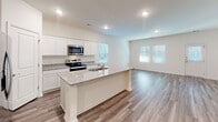 Located at 4236 Hollow Wind Way in Summerville, SC, this single-story home presents a clean, modern interior designed for comfortable everyday living. The open-concept layout connects the kitchen and living areas seamlessly, with wood-look luxury vinyl plank flooring extending throughout the main living spaces and recessed lighting illuminating the interiors.

The kitchen is a standout feature, equipped with white shaker-style cabinetry, granite countertops, and a full suite of stainless steel appliances including a refrigerator with ice maker, electric range, and built-in microwave. A central island with an integrated sink provides additional workspace and casual seating, while windows overlooking the living area allow natural light to flow freely throughout.

The bedrooms are carpeted for comfort, with windows admitting natural light and generous closet space, including a walk-in closet outfitted with wire shelving systems. The primary bathroom offers a double vanity with white cabinetry, a framed walk-in shower with glass doors, and wood-look flooring. A secondary bathroom features a single vanity with a mirror and classic fixtures. A dedicated laundry area with wire shelving and utility hookups rounds out this well-organized home.