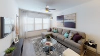 Located in Davenport, Florida, this single-floor residence offers a thoughtfully designed open-concept layout that seamlessly connects the kitchen, dining, and living areas. The kitchen is a standout space, showcasing rich dark wood cabinetry, granite countertops, a large center island with a double undermount sink and pendant lighting overhead, and a full suite of stainless steel appliances including a refrigerator, range, microwave, and dishwasher. Wood-look flooring flows throughout the main living areas, adding warmth and continuity to the space. The living room is bright and welcoming, featuring large windows with blinds that allow ample natural light, a ceiling fan, and generous room for comfortable seating. A dedicated dining area with a round table sits adjacent to the kitchen, making the layout ideal for entertaining. The bedrooms offer plush carpeting, ceiling fans, and windows dressed with curtains and blinds, providing a calm and restful retreat. The bathrooms are finished with granite-topped vanities, wood-look flooring, and a bathtub with shower combination. Throughout the residence, clean white walls and consistent modern finishes create a cohesive and contemporary aesthetic.