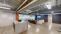 Located at 300 18th St S in Birmingham, Alabama, this single-floor commercial space blends industrial architecture with contemporary design to create a dynamic and functional environment. Polished concrete floors run throughout, complementing the exposed ceiling structure where ductwork, piping, and acoustic spray finish are left intentionally visible, lending an authentic urban character to the space.

The open layout centers around a spacious lounge and collaboration zone furnished with a mix of leather and upholstered seating, area rugs, and a wall-mounted display screen, making it ideal for both casual gatherings and presentations. A striking marble-surfaced reception counter anchors one end of the main area, while a decorative glass and metal railing partition delineates an interior overlook zone, adding architectural depth.

A dedicated conference area features a large oval wood table surrounded by upholstered chairs, set atop a bold patterned rug beneath the open ceiling. The kitchenette is well-appointed with dark countertops, gray cabinetry, a dual-basin sink, a beverage refrigerator, and a Keurig station, accented by a vibrant multicolored geometric mural that energizes the space. Bold accent walls in teal, orange, and navy add visual interest throughout, while accent lighting and large windows contribute to a bright, inviting atmosphere suited for a modern professional setting.