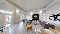 This single-story clubhouse offers a thoughtfully designed community space that balances social gathering areas with fitness amenities. The combined dining and living room serves as the heart of the clubhouse, featuring soaring ceilings, crown molding, and decorative columns that lend a classic architectural character. A striking arched accent wall clad in dark shiplap houses a mounted flat-screen TV and a floating shelf, creating a dramatic focal point. Large French doors and transom windows flood the space with natural light, while light hardwood flooring and a neutral palette maintain an airy, welcoming atmosphere. A shuffleboard table adds a recreational touch to the lounge area. The hallway connects the spaces with refined finishes, including large-format tile flooring and elegant arched doorways adorned with curated artwork. The exercise room is generously sized and well-equipped with treadmills, an elliptical, a rowing machine, a cable machine, free weights, and kettlebells, complemented by ceiling fans, full-length mirrors, and a mounted TV. The kitchen is outfitted with stainless steel appliances, crisp white cabinetry, quartz countertops, a dark island, and a bold black-and-white hexagonal mosaic tile backsplash that extends to the ceiling, adding a distinctive modern flair.