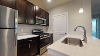 Located at 1000 Solomon Sq in Delaware, Ohio, this single-floor residence offers a well-designed, open-concept layout that balances modern finishes with functional living spaces. The kitchen serves as a central highlight, featuring rich dark cabinetry, light quartz countertops, a stainless steel sink, and a full suite of stainless steel appliances including a gas range, over-the-range microwave, and refrigerator. Pendant lighting adds a polished touch above the kitchen area, which flows seamlessly into the main living space via a breakfast bar-style peninsula. The living area is spacious and open, finished with durable hardwood-style flooring and neutral-toned walls that create a bright, welcoming atmosphere. A dedicated entryway with a paneled white door provides a clean transition into the home. The bedrooms are carpeted for comfort and feature large windows that invite natural light and offer pleasant outdoor views, along with sliding-door closets for ample storage. The bathroom is outfitted with dark cabinetry, a quartz vanity top, a framed mirror, and a shower-tub combination, maintaining the same cohesive, contemporary aesthetic found throughout the rest of the home.