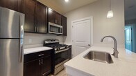 Located at 1000 Solomon Sq in Delaware, Ohio, this single-floor residence offers a well-designed, open-concept layout that balances modern finishes with functional living spaces. The kitchen serves as a central highlight, featuring rich dark cabinetry, light quartz countertops, a stainless steel sink, and a full suite of stainless steel appliances including a gas range, over-the-range microwave, and refrigerator. Pendant lighting adds a polished touch above the kitchen area, which flows seamlessly into the main living space via a breakfast bar-style peninsula. The living area is spacious and open, finished with durable hardwood-style flooring and neutral-toned walls that create a bright, welcoming atmosphere. A dedicated entryway with a paneled white door provides a clean transition into the home. The bedrooms are carpeted for comfort and feature large windows that invite natural light and offer pleasant outdoor views, along with sliding-door closets for ample storage. The bathroom is outfitted with dark cabinetry, a quartz vanity top, a framed mirror, and a shower-tub combination, maintaining the same cohesive, contemporary aesthetic found throughout the rest of the home.