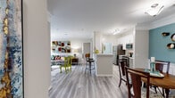 This single-floor residence at Monticello Mews in Hampton, Virginia offers a thoughtfully designed open-concept layout with stylish finishes throughout. The living room serves as the heart of the home, anchored by a classic fireplace with a built-in arched display niche and sliding glass doors that open to a private balcony with outdoor views. Light-toned hardwood-style flooring flows seamlessly through the main living areas, complementing the neutral color palette.

The kitchen is well-equipped with white shaker cabinetry, subway tile backsplash, stainless steel appliances, and ample counter space, with direct access to a dedicated in-unit laundry room. A peninsula with bar seating connects the kitchen to the open living and dining areas. The dining room features elegant wainscoting, crown molding, and a teal accent wall, adding a refined touch to the space.

The bedrooms offer plush carpeting and generous natural light through large windows, with waterfront views visible from one of the rooms. The bathroom is clean and functional, featuring a white vanity and hardwood-style flooring. A built-in desk nook provides a convenient workspace within the home. Crown molding throughout the main living areas adds a polished, classic architectural detail to this comfortable and cohesive residence.