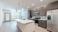 Located in the desirable Lakewood Ranch community of Sarasota, Florida, this well-appointed one-bedroom, one-bathroom residence offers a thoughtfully designed layout with modern finishes throughout. The open-concept kitchen and living area serves as the heart of the home, featuring light wood-style flooring, a large central island with a white quartz countertop and undermount sink, and pendant lighting overhead. The kitchen is outfitted with dark espresso-toned cabinetry extending to the ceiling, a mosaic tile backsplash, and a full suite of stainless steel appliances including a French door refrigerator, range, microwave, and dishwasher. The living area flows seamlessly from the kitchen, bathed in natural light from large windows with blinds and finished with a ceiling fan. The bedroom is a comfortable retreat with plush carpeting, a ceiling fan, and a bright window. A dedicated closet provides ample storage. The bathroom features large-format tile flooring, a double-sink vanity with quartz countertops, backlit mirrors, and a soaking tub with a tiled surround. Clean lines, neutral tones, and quality materials define the overall ambiance of this contemporary residence.