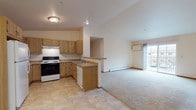 Located at 3225 Whiting Ave in Stevens Point, Wisconsin, this single-floor residence offers a well-organized and functional layout designed for comfortable everyday living. The open-concept kitchen and living area serves as the heart of the space, with the kitchen featuring warm oak cabinetry, ample counter space, a built-in range with overhead ventilation, a dishwasher, and a double sink. A peninsula counter provides a natural transition into the carpeted living area, which is brightened by a sliding glass door that opens to a balcony and allows generous natural light to fill the room. A ceiling fan and wall-mounted air conditioning unit add to the comfort of the living space, while baseboard heating is present throughout. The bedrooms are generously sized with plush carpeting, large windows that bring in natural light, and closet access via wood-paneled doors. Two bathrooms serve the residence — one featuring a walk-in shower stall with a single-sink vanity and tile flooring, and a second, more spacious bathroom with an extended vanity, large mirror, and a separate water closet area. Neutral tones, warm wood accents, and tile flooring in the kitchen and bathrooms contribute to a clean, cohesive aesthetic throughout the entire space.