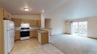 Located at 3225 Whiting Ave in Stevens Point, Wisconsin, this single-floor residence offers a well-organized and functional layout designed for comfortable everyday living. The open-concept kitchen and living area serves as the heart of the space, with the kitchen featuring warm oak cabinetry, ample counter space, a built-in range with overhead ventilation, a dishwasher, and a double sink. A peninsula counter provides a natural transition into the carpeted living area, which is brightened by a sliding glass door that opens to a balcony and allows generous natural light to fill the room. A ceiling fan and wall-mounted air conditioning unit add to the comfort of the living space, while baseboard heating is present throughout. The bedrooms are generously sized with plush carpeting, large windows that bring in natural light, and closet access via wood-paneled doors. Two bathrooms serve the residence — one featuring a walk-in shower stall with a single-sink vanity and tile flooring, and a second, more spacious bathroom with an extended vanity, large mirror, and a separate water closet area. Neutral tones, warm wood accents, and tile flooring in the kitchen and bathrooms contribute to a clean, cohesive aesthetic throughout the entire space.