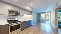 Located in the vibrant Little Italy neighborhood of San Diego, this thoughtfully designed one-bedroom, one-bathroom apartment at 2155 Kettner Blvd offers a clean, modern aesthetic throughout. The open-concept kitchen and living area serves as the heart of the unit, featuring warm wood-look flooring, recessed lighting, and a seamless flow toward a private balcony with sliding glass door that invites abundant natural light. The well-appointed kitchen is outfitted with stainless steel appliances — including a gas range, microwave, dishwasher, and French door refrigerator — paired with two-tone cabinetry in gray and taupe, white subway tile backsplash, and light quartz countertops. The bedroom offers plush striped carpeting, neutral wall tones, and a bright window with outdoor views. A dedicated walk-in closet with built-in shelving and hanging rods provides generous storage. The bathroom features large-format tile flooring, a rich espresso-toned vanity with white countertop, a wide mirror, and a glass-enclosed shower. Clean lines and a cohesive neutral palette give the entire space a contemporary, move-in-ready feel well suited to urban San Diego living.