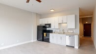 This single-floor unit offers a clean, modern layout designed for comfortable everyday living. The open-concept main area seamlessly blends the living space and kitchen, creating an airy, functional environment bathed in natural light. Light wood-look luxury vinyl flooring runs throughout, lending a warm yet contemporary feel to the space.

The kitchen is well-equipped with crisp white shaker-style cabinetry extending to the ceiling for ample storage, black appliances including a refrigerator, electric range, and built-in microwave, as well as a stainless steel dishwasher and a single-basin sink with a modern faucet. Light countertops complement the white cabinetry, keeping the aesthetic clean and cohesive. A ceiling fan with a built-in light fixture anchors the living area, providing both airflow and ambient lighting.

The bathroom showcases thoughtful design with a soaking tub and shower combination, featuring a striking mosaic tile surround in neutral earth tones alongside wood-look tile accents, adding a spa-inspired touch. Brushed nickel fixtures complete the refined look.

The floor plan, visible through the dollhouse view, reveals a compact yet efficiently organized layout with clearly defined zones for living, cooking, and bathing, making excellent use of the available space throughout.