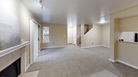 Located at 3120 NE John Olsen Ave in Hillsboro, Oregon, this two-story, two-bedroom, two-bathroom home offers a practical and comfortable layout spread across two floors. The main level features a generously sized combined living and dining area with warm neutral tones, plush carpeting, and a classic tile-surround fireplace with a white mantel that serves as the room's focal point. Natural light filters in through multiple windows, and a sliding glass door opens directly to a private patio. The kitchen is efficiently designed with ample cabinetry featuring wood-trim accents, white countertops, a full suite of appliances including a black refrigerator and electric range, and durable wood-look flooring. A dedicated laundry area houses a full-size side-by-side washer and dryer. Upstairs, the primary bedroom offers a comfortable footprint with a large closet and a bright window with outdoor views. The second bedroom is equally well-appointed with carpeting and closet storage. Both bathrooms feature wood-look flooring, vanities with large mirrors, and tub-shower combinations. Four closets throughout the home provide abundant storage. A hallway and two staircases complete the thoughtful two-floor layout.