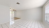 Located at 6919 Julia Court in New Port Richey, Florida, this single-story, 2-bedroom, 1-bathroom home offers a clean and functional layout throughout. The bright living room welcomes you with gleaming white tile flooring, neutral white walls, and a front-facing window that fills the space with natural light. A ceiling fan overhead adds comfort to the open living area, which flows directly into the galley-style kitchen. The kitchen is well-appointed with ample white cabinetry lining both walls, light countertops, a double sink, and an electric range — all illuminated by a skylight panel above. Louvered bifold doors conceal additional storage within the kitchen. Both bedrooms feature light wood-look flooring and windows with views of the surrounding greenery. The primary bedroom includes a generously sized walk-in closet with multi-rail shelving, offering excellent storage capacity. The second bedroom is served by a louvered bifold closet. The shared full bathroom includes a tub/shower combination, a vanity with storage below, and a wide mirror. Outside, the private backyard is enclosed by a wooden privacy fence and shaded by mature trees and palms, creating a peaceful outdoor retreat. A central air conditioning unit services the home.