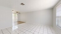 Located at 6919 Julia Court in New Port Richey, Florida, this single-story, 2-bedroom, 1-bathroom home offers a clean and functional layout throughout. The bright living room welcomes you with gleaming white tile flooring, neutral white walls, and a front-facing window that fills the space with natural light. A ceiling fan overhead adds comfort to the open living area, which flows directly into the galley-style kitchen. The kitchen is well-appointed with ample white cabinetry lining both walls, light countertops, a double sink, and an electric range — all illuminated by a skylight panel above. Louvered bifold doors conceal additional storage within the kitchen. Both bedrooms feature light wood-look flooring and windows with views of the surrounding greenery. The primary bedroom includes a generously sized walk-in closet with multi-rail shelving, offering excellent storage capacity. The second bedroom is served by a louvered bifold closet. The shared full bathroom includes a tub/shower combination, a vanity with storage below, and a wide mirror. Outside, the private backyard is enclosed by a wooden privacy fence and shaded by mature trees and palms, creating a peaceful outdoor retreat. A central air conditioning unit services the home.
