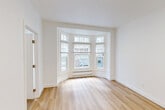 Located in San Francisco's Lower Nob Hill neighborhood, this one-bedroom, one-bathroom residence offers a thoughtfully laid-out floor plan across a single level. The living room is a standout feature, highlighted by a classic angled bay window that floods the space with natural light and frames views of the surrounding streetscape. Light-toned hardwood floors run throughout the main living areas, contributing to a bright and airy atmosphere complemented by crisp white walls and clean white trim.

A hallway connects the living room to the remaining rooms, providing a sense of flow throughout the unit. The kitchen is efficiently designed, featuring white shaker-style cabinetry, marble-patterned countertops, a stainless steel sink, and a white electric range with a ventilation hood overhead — offering a clean, functional workspace. The bedroom is carpeted for comfort and includes a window with a baseboard heater beneath it, providing views of the neighboring brick building. The bathroom is neatly appointed with a white vanity, a mirrored medicine cabinet, a lighted vanity fixture, and hardwood-style flooring. A connecting hallway completes the layout, making this a well-organized and efficiently designed urban residence.