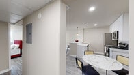 This well-designed one-bedroom, one-bathroom unit offers a thoughtfully organized layout across a single floor. The open-concept kitchen and living area serves as the heart of the space, featuring a sleek white kitchen with tall cabinetry, quartz countertops, and a full suite of stainless steel appliances including a refrigerator, range, and microwave. A peninsula with bar seating provides additional dining options and separates the kitchen from the living area, which is illuminated by recessed lighting and a stylish woven pendant light. Light-tone wood-look flooring flows consistently throughout, adding cohesion and warmth.

The living area offers generous room for furnishings and benefits from a window allowing natural light. A hallway connects the main living space to the private quarters, featuring a dedicated closet for storage. The bedroom is a well-proportioned retreat with its own window and ceiling light fixture, complemented by neutral walls and the same durable flooring. The bathroom is finished with floor-to-ceiling gray stone-look tile, a tub-shower combination, and marble-style tile flooring, creating a clean, polished aesthetic. Overall, the unit presents a modern, minimalist design suited for comfortable everyday living.