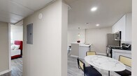 This well-designed one-bedroom, one-bathroom unit offers a thoughtfully organized layout across a single floor. The open-concept kitchen and living area serves as the heart of the space, featuring a sleek white kitchen with tall cabinetry, quartz countertops, and a full suite of stainless steel appliances including a refrigerator, range, and microwave. A peninsula with bar seating provides additional dining options and separates the kitchen from the living area, which is illuminated by recessed lighting and a stylish woven pendant light. Light-tone wood-look flooring flows consistently throughout, adding cohesion and warmth.

The living area offers generous room for furnishings and benefits from a window allowing natural light. A hallway connects the main living space to the private quarters, featuring a dedicated closet for storage. The bedroom is a well-proportioned retreat with its own window and ceiling light fixture, complemented by neutral walls and the same durable flooring. The bathroom is finished with floor-to-ceiling gray stone-look tile, a tub-shower combination, and marble-style tile flooring, creating a clean, polished aesthetic. Overall, the unit presents a modern, minimalist design suited for comfortable everyday living.