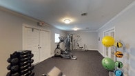 This dedicated fitness space is thoughtfully designed to support a comprehensive workout routine. The room features durable speckled rubber flooring throughout, providing a safe and functional surface for all types of exercise. Crown molding and light gray walls lend a clean, polished aesthetic that elevates the space beyond a typical gym setting.

The layout accommodates a diverse array of equipment, including a treadmill, elliptical trainer, stationary bike, and a multi-station cable weight machine, alongside a dedicated bench press and adjustable weight bench. A rack of hex dumbbells in varying sizes offers options for free weight training, while a standing medicine ball rack stocked with multiple weighted balls adds versatility for functional fitness exercises. Stability balls are also present for core and flexibility work.

Natural light filters in through multiple windows fitted with white blinds, keeping the space bright and well-ventilated. Flush-mount ceiling light fixtures provide consistent overhead illumination. The room is accessible through both a set of French doors with glass panels and a standard double-panel door, with an emergency exit also clearly marked. Wall-mounted HVAC vents ensure comfortable temperature regulation during workouts. Overall, this fitness room delivers a well-rounded, professional-grade exercise environment in a refined and welcoming setting.