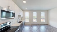This contemporary single-floor unit showcases a clean, modern design throughout. The open-concept layout seamlessly connects the kitchen and living area, creating a bright and airy atmosphere enhanced by large double-hung windows that flood the space with natural light and offer views of the surrounding neighborhood. Wood-look plank flooring runs throughout, tying the spaces together cohesively.

The kitchen is a standout feature, outfitted with a two-tone cabinetry scheme pairing crisp white upper cabinets with wood-grain lower cabinets. A suite of stainless steel appliances includes a refrigerator, electric range, built-in microwave, and dishwasher, all complemented by light quartz countertops and a stainless steel sink. Recessed and flush-panel ceiling lighting provides well-distributed illumination.

The bathroom continues the unit's modern aesthetic with white cabinetry, a sleek white vanity countertop, a large mirror, and wood-look tile flooring, creating a clean and functional space. A dedicated utility area houses a stacked washer and dryer unit alongside built-in wire shelving, offering convenient in-unit laundry and additional storage. Overall, the unit presents a polished, move-in-ready living environment with thoughtful finishes throughout.