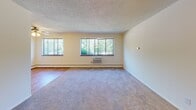 Located at 110 Daniel Dr in Webster, NY, this single-floor unit offers a practical and comfortable layout spread across several well-defined living areas. The spacious living room is a standout feature, boasting a bank of large windows that frame lush greenery outside, flooding the room with natural light. The living area features a combination of hardwood-style flooring and plush carpeting, with a wall-mounted air conditioning unit and baseboard heating for year-round comfort. The unit includes multiple rooms, each equipped with ceiling fans and windows that invite in natural light and outdoor views. Some rooms feature soft carpeting underfoot, while others showcase warm wood-tone flooring, adding visual variety throughout the space. The kitchen is efficiently designed with warm wood cabinetry, a double-basin sink, and white appliances including a refrigerator and electric range with overhead ventilation. Baseboard heating runs throughout the unit, complemented by textured ceilings that add a classic touch. The overall ambiance is clean, bright, and move-in ready, offering a comfortable living environment in a quiet Webster, NY location.