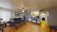 This single-floor residence offers a thoughtfully designed layout that maximizes both comfort and functionality. The open-concept living and dining area serves as the heart of the home, featuring warm hardwood-style flooring, neutral walls, and a ceiling fan with integrated lighting. Large windows allow natural light to fill the space, while a glass-top coffee table and plush sofa create an inviting atmosphere for relaxing or entertaining. Framed artwork on the walls adds a personal touch to the living area.

The galley-style kitchen is efficiently laid out with light wood cabinetry, granite-style countertops, a double sink, a dishwasher, a full-size refrigerator, and a black electric range. The kitchen opens toward the living space, maintaining a sense of connectivity throughout.

A compact dining area adjacent to the entryway features a sliding glass door that opens to a private patio, bringing in additional natural light and offering a seamless indoor-outdoor connection.

The bedroom is a comfortable retreat finished with plush carpeting, a window with decorative curtains, and direct access to a spacious walk-in closet. The full bathroom includes a dark wood vanity with granite-style countertop, a large mirror, and a shower-tub combination.