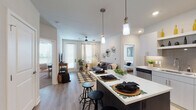 This thoughtfully designed single-floor residence offers a seamless open-concept layout that connects the kitchen, dining, and living areas into one cohesive space. The kitchen is outfitted with white cabinetry, white quartz countertops, a stainless steel dishwasher, and a large island with bar seating illuminated by stylish pendant lighting — ideal for casual dining and entertaining. Light wood-style flooring runs throughout the main living areas, enhancing the bright, airy atmosphere created by large windows dressed with sheer curtains and blinds.

The living room provides a comfortable retreat with a ceiling fan, direct access to an exterior door, and ample natural light. The primary bedroom features plush carpeting, a ceiling fan, large windows, and warm wood-toned built-in nightstands, complemented by a walk-in closet. A second bedroom offers versatile use with carpet flooring, a ceiling fan, natural light, and an adjacent walk-in closet. The shared bathroom includes a dual-sink vanity with wood-toned cabinetry, a large framed mirror with vanity lighting, and wood-style flooring. Throughout the space, neutral tones and modern fixtures contribute to a clean, contemporary aesthetic.